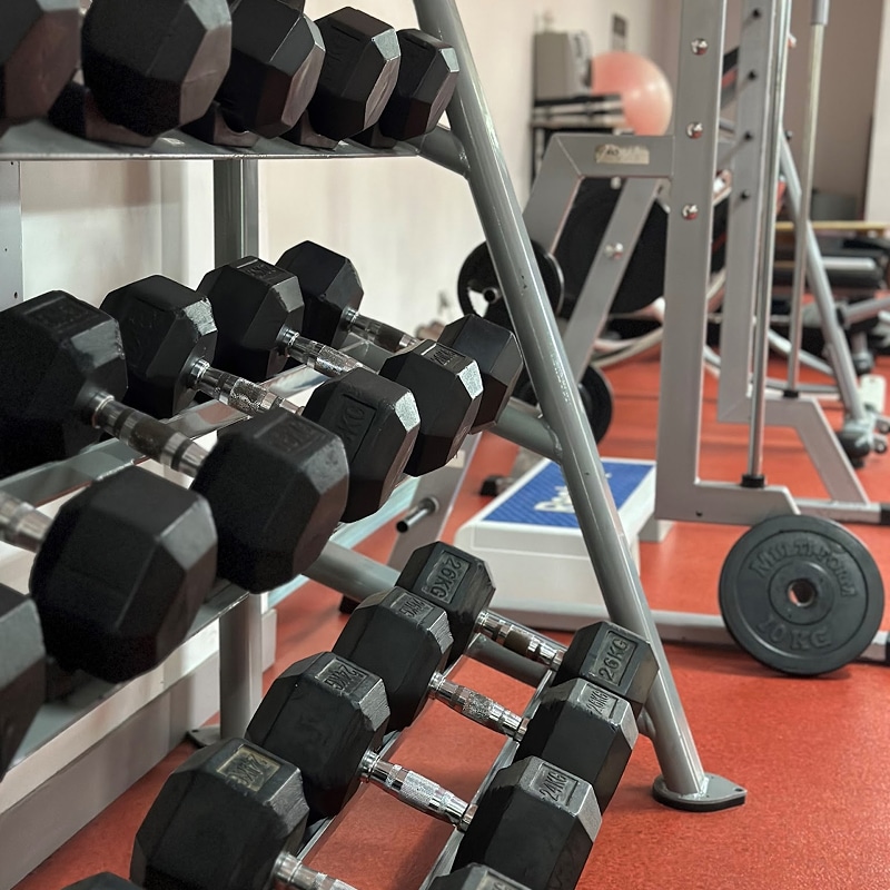 Dumbbells Musculation: Haltères Hexagonaux sur Rack Rangement de dumbbells hexagonaux noirs, étiquetés '26KG' et '24KG', dans une salle de sport avec sol rouge et équipement de musculation en arrière-plan.