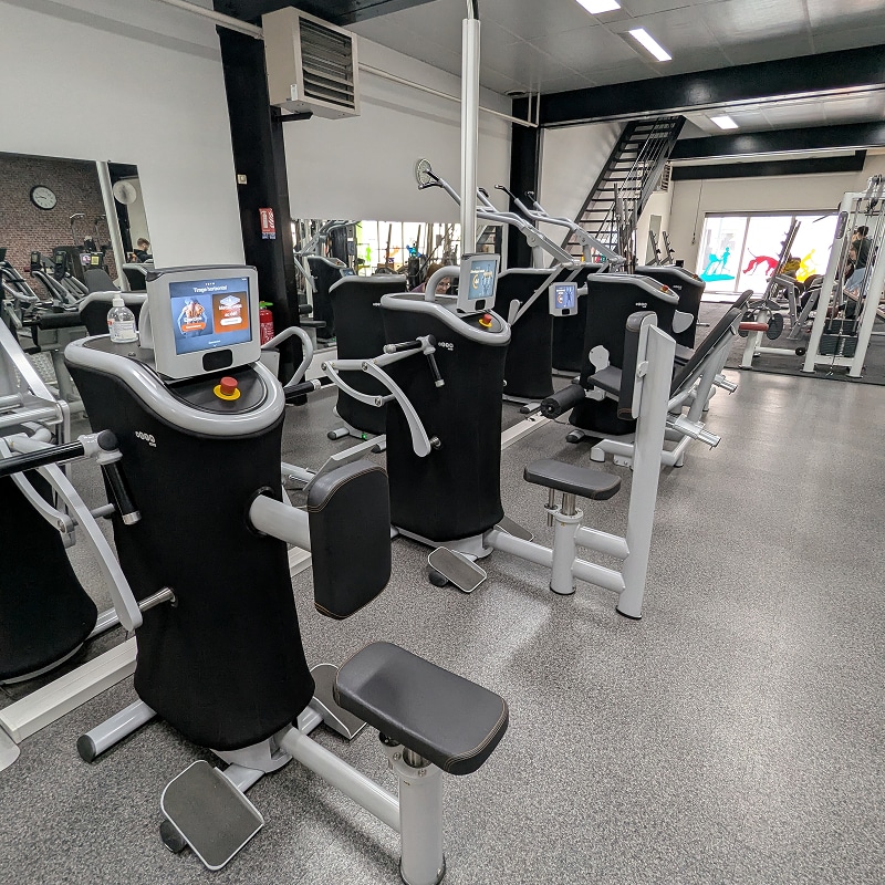 Machines de musculation EGYM en salle de sport moderne Intérieur d'une salle de sport moderne avec plusieurs machines d'entraînement cardio et musculation high-tech de marque EGYM, affichant un écran tactile avec l'instruction "Travail musculaire".