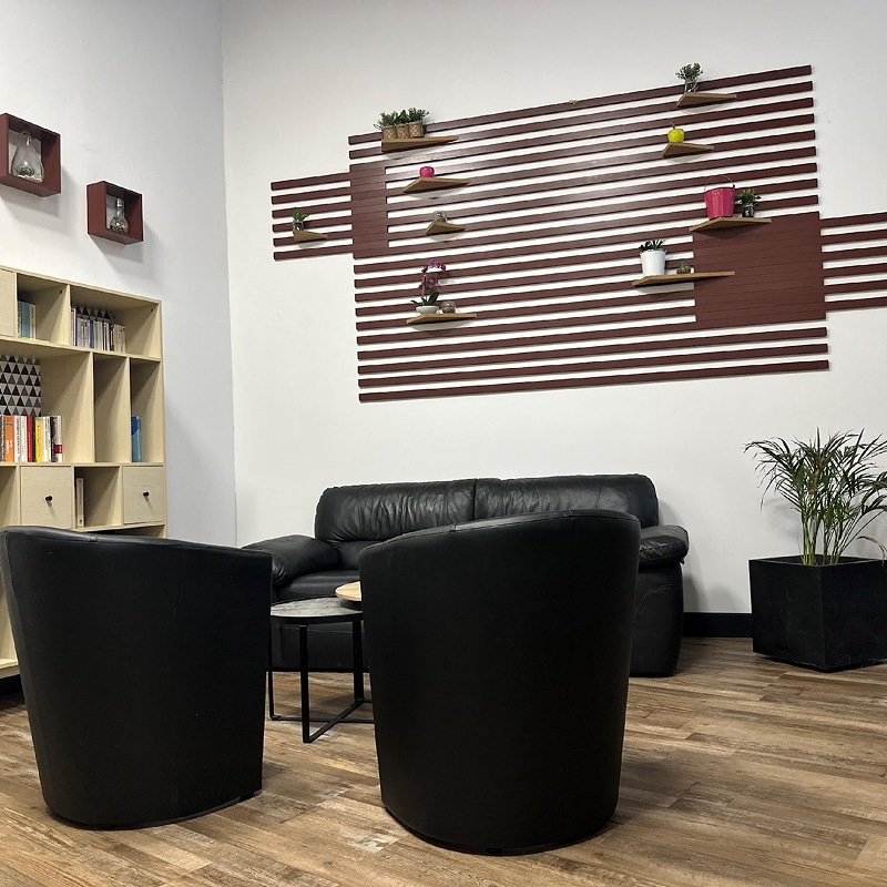 Salon Bureau Moderne: Cuir Noir et Déco Murale Coin salon moderne avec canapé et fauteuils noirs en cuir, étagères murales décoratives marron à rayures, et bibliothèque claire.